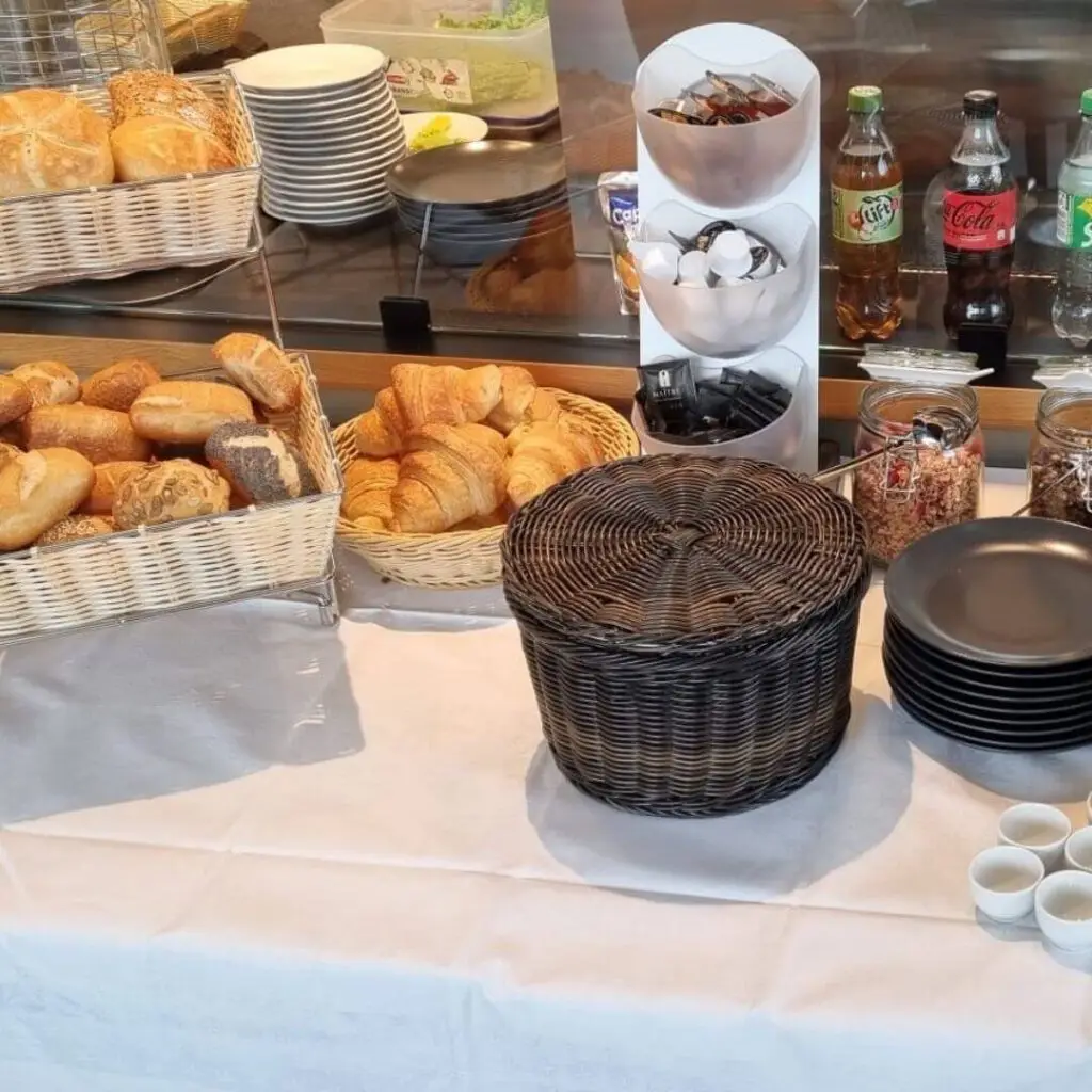 Frühstücksbuffet mit frischen Brötchen, Croissants, Backwaren, Körben, Müsligläsern und Getränken