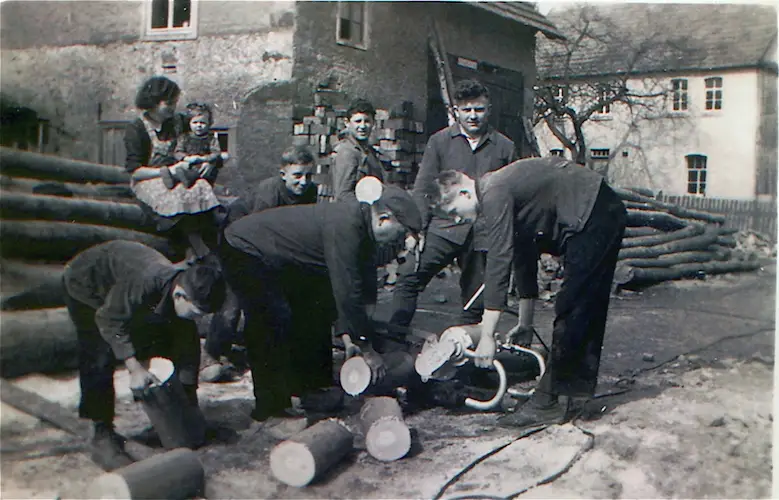 Historisches Schwarzweißfoto: Männer und Jungen bei Holzarbeiten, Sägen und Stapeln von Baumstämmen im Dorfhof