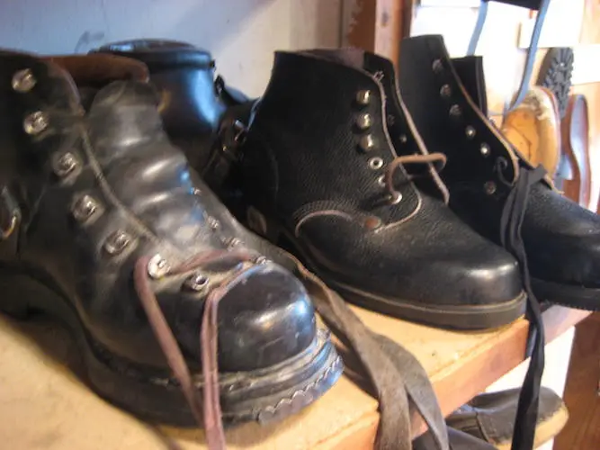 Gebrauchte schwarze Lederstiefel und Arbeitsschuhe auf Holzregal, vintage Outdoor-Stiefel