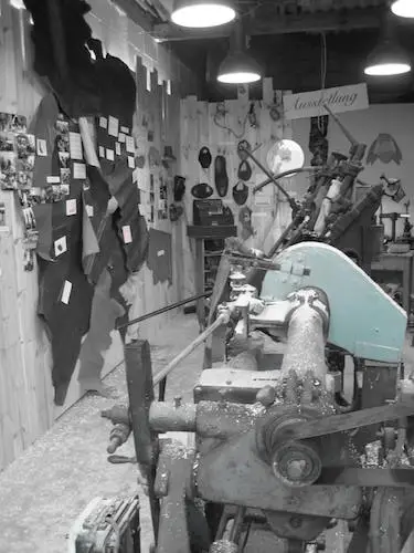 Schwarzweiß-Foto einer historischen Werkstatt mit alter Drehmaschine, Werkzeugen und an der Wand gehängten Tierhäuten