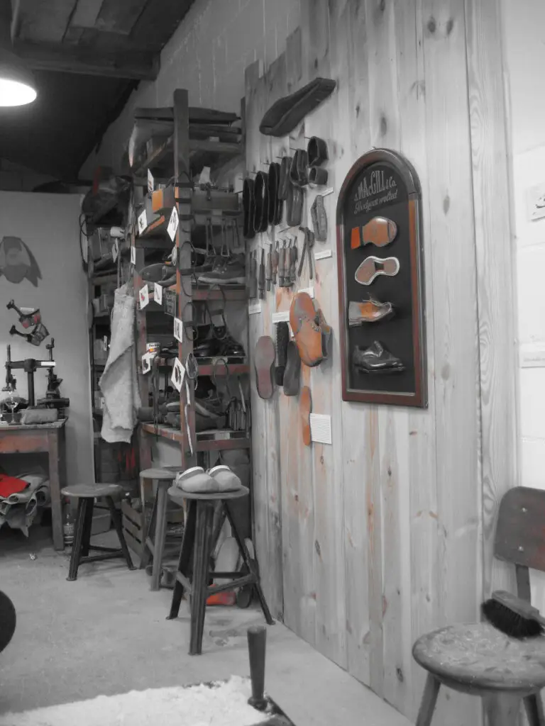 Schusterwerkstatt: Innenansicht mit Holzverkleidung, Schuhleisten, Ledersohlen, Werkzeugen und Werkbänken