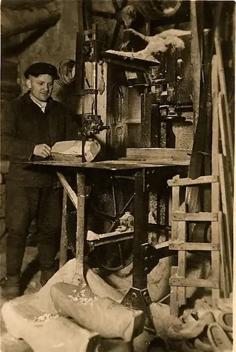 Historische Werkstatt: Tischler an Bandsäge beim Zuschneiden von Holz, Sägespäne und Werkzeuge im Umfeld