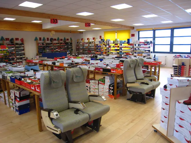 Großes Schuhoutlet mit Regalen voller Schuhkartons, Ausstellungstische und Flugzeugsitze als Sitzprobe